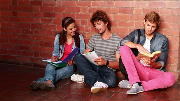 Studenti seduti contro il muro che leggono libri di testo.