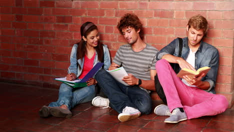 students sitting against wall reading textbooks