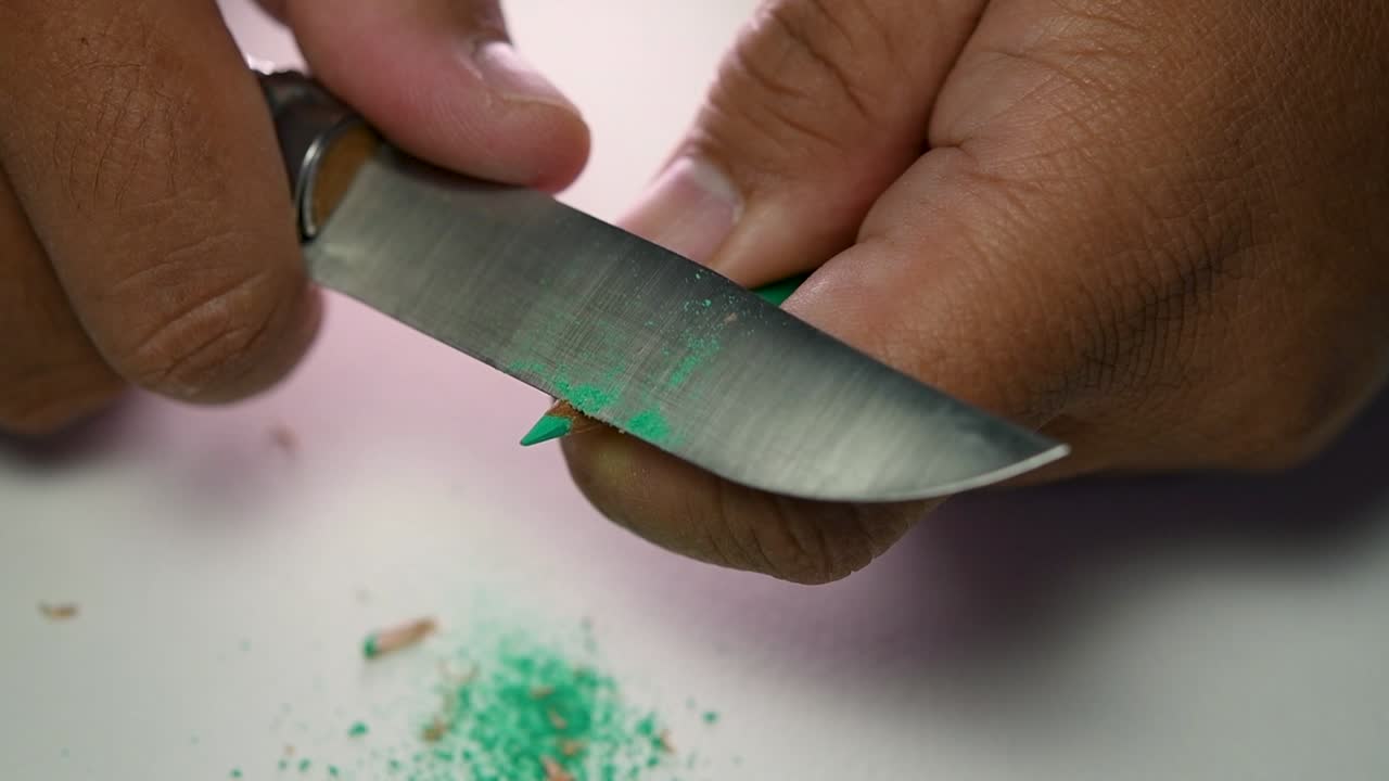 날카로운 칼로 연필과 색연필을 천천히 갈고 있는 손의 영상