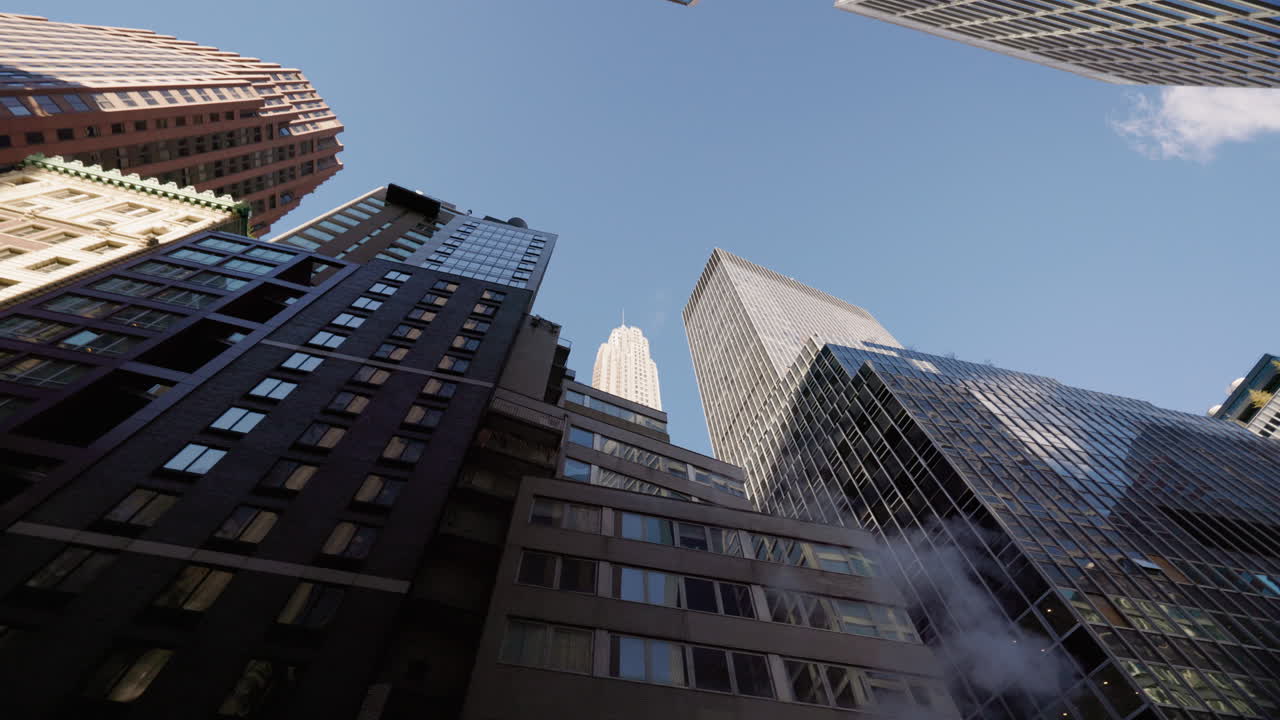 Grattacieli che si ergono sopra le strade di Manhattan a New York City, una vista drammatica dal basso con vapore e moderne torri per uffici sotto un cielo blu, USA.