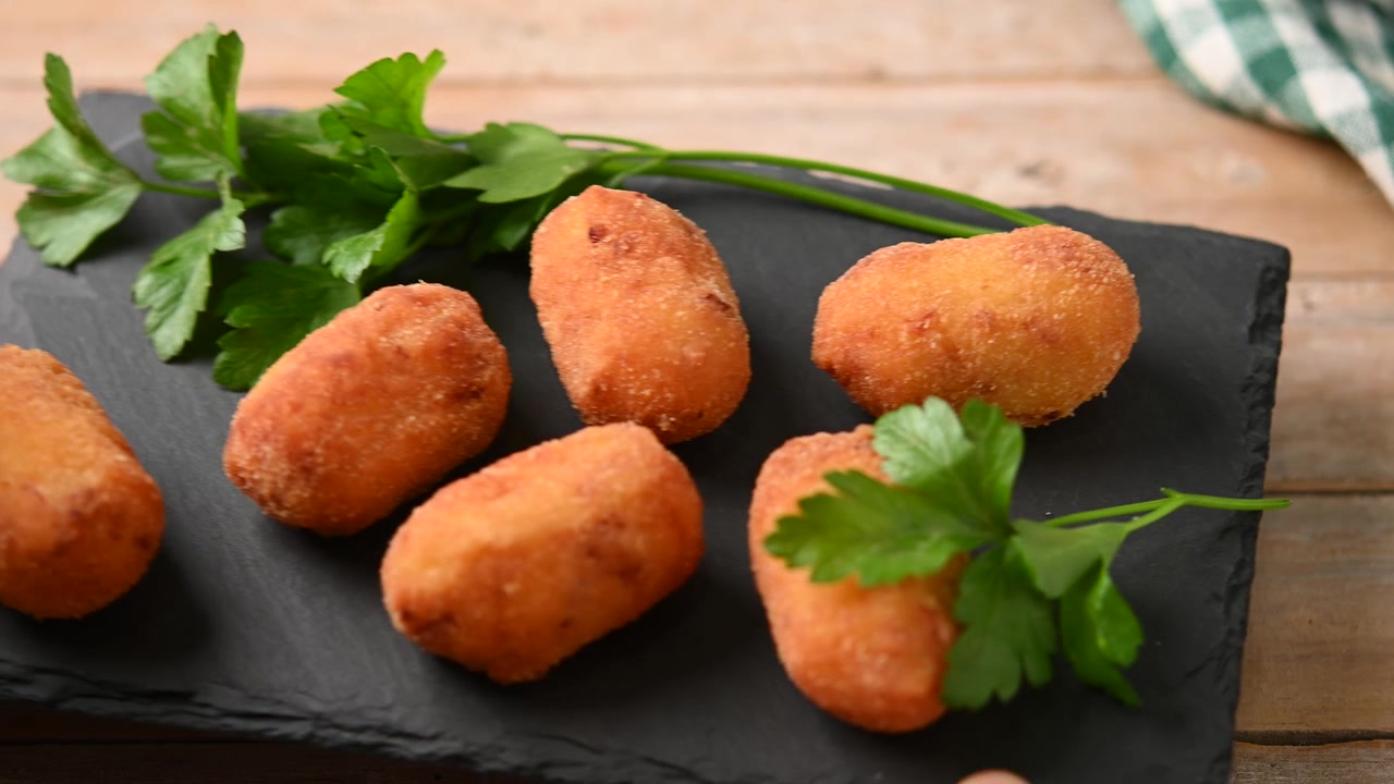 Mano che posiziona un vassoio di ardesia con crocchette fritte su un tavolo di legno