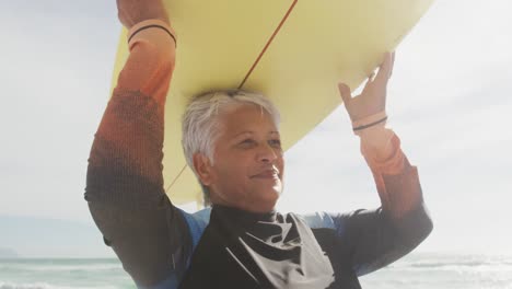 happy senior hispanic woman walking on beach with surfboard over head