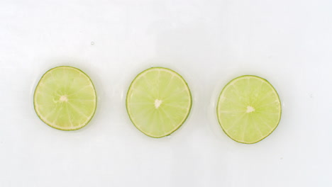 drops of water fall on three pieces of lime lying on a white background.