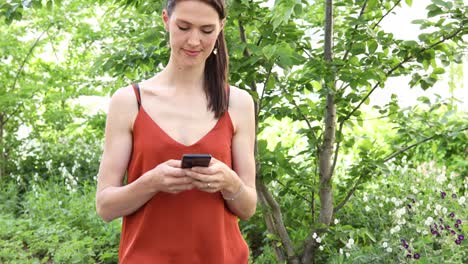 a young german woman with long brown hair is standing outside and typing on her smartphone or mobile phone