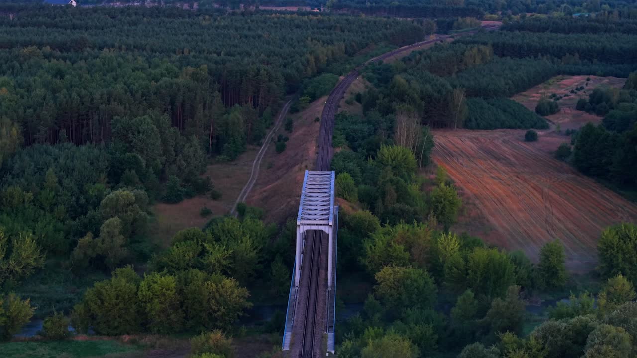 Aerial establishing shot of old steel bridge in polish countryside. Forest landscape at sunrise. Flyover shot. Railway and tracks in suburbia