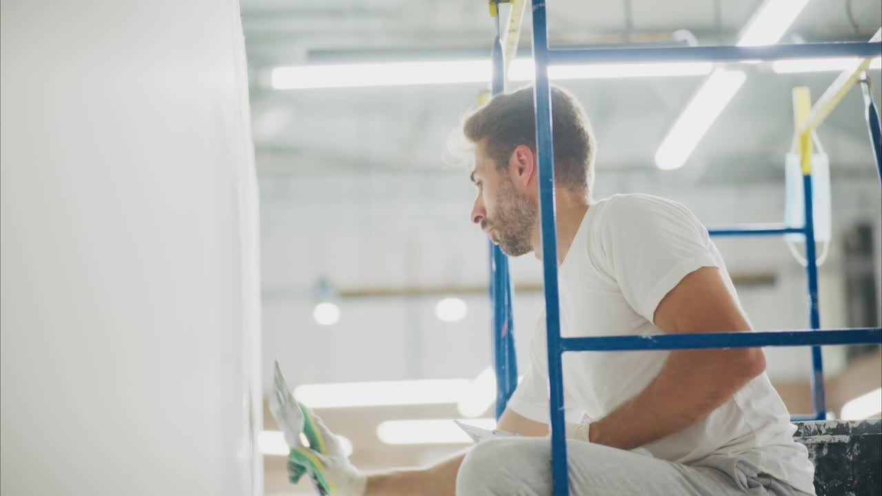 Ein erfahrener Maler auf einem Gerüst, der präzise arbeitet und sorgfältig den letzten Schliff auf eine frische Farbschicht an einer Wand in einer gut beleuchteten Umgebung aufträgt