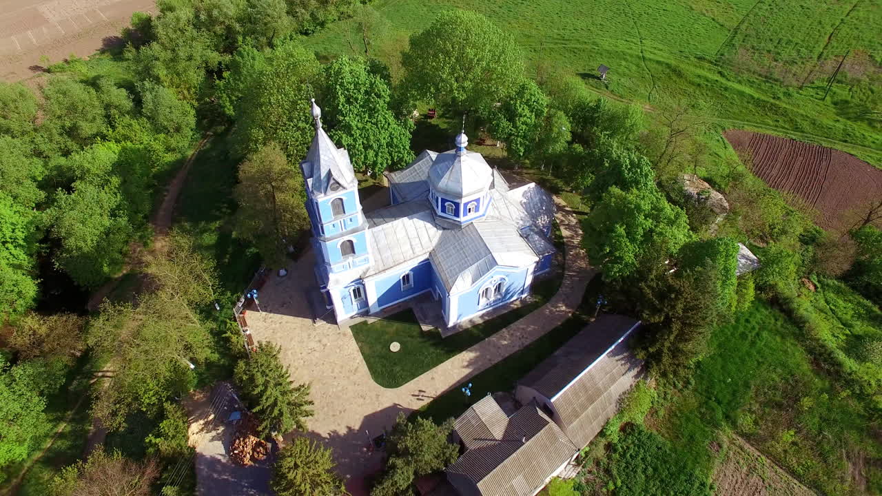 Beautiful building of a church surrounded by green trees. Drone circle movement over the building lit by bright sunshine. Top view.