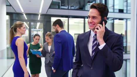 Businessman-talking-on-mobile-phone-and-colleague-discussing-in-background