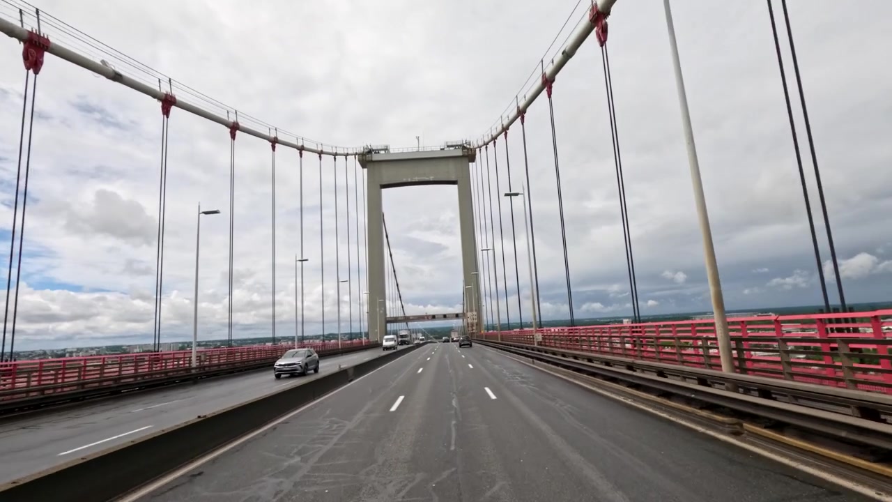 Prospettiva dinamica della telecamera del traffico che attraversa un ponte sospeso sotto un cielo nuvoloso