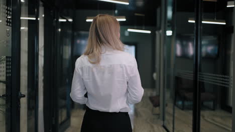 the camera follows the back of a blonde business woman in a shirt down the corridor