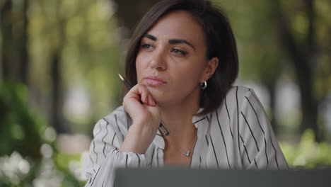 Pensive-woman-Brunette-Hispanic-ethnic-group-sits-at-a-table-in-a-summer-cafe-with-a-laptop.-Serious-business-woman-pondering-problem-solving-and-business-development-strategy