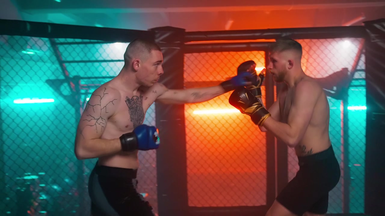 Dois boxeadores treinando em uma jaula de academia iluminada por neon