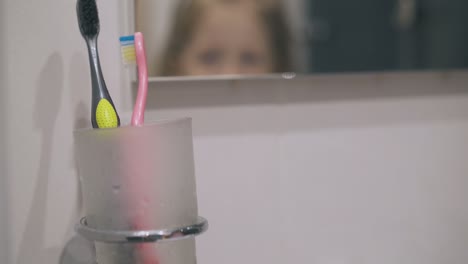 une petite fille met une brosse à dents dans un porte-verre dans la salle de bain.