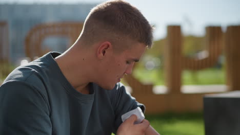 side view of young boy gently placing nicotine patch on upper arm while seated outdoors under bright sunlight with soft blur background