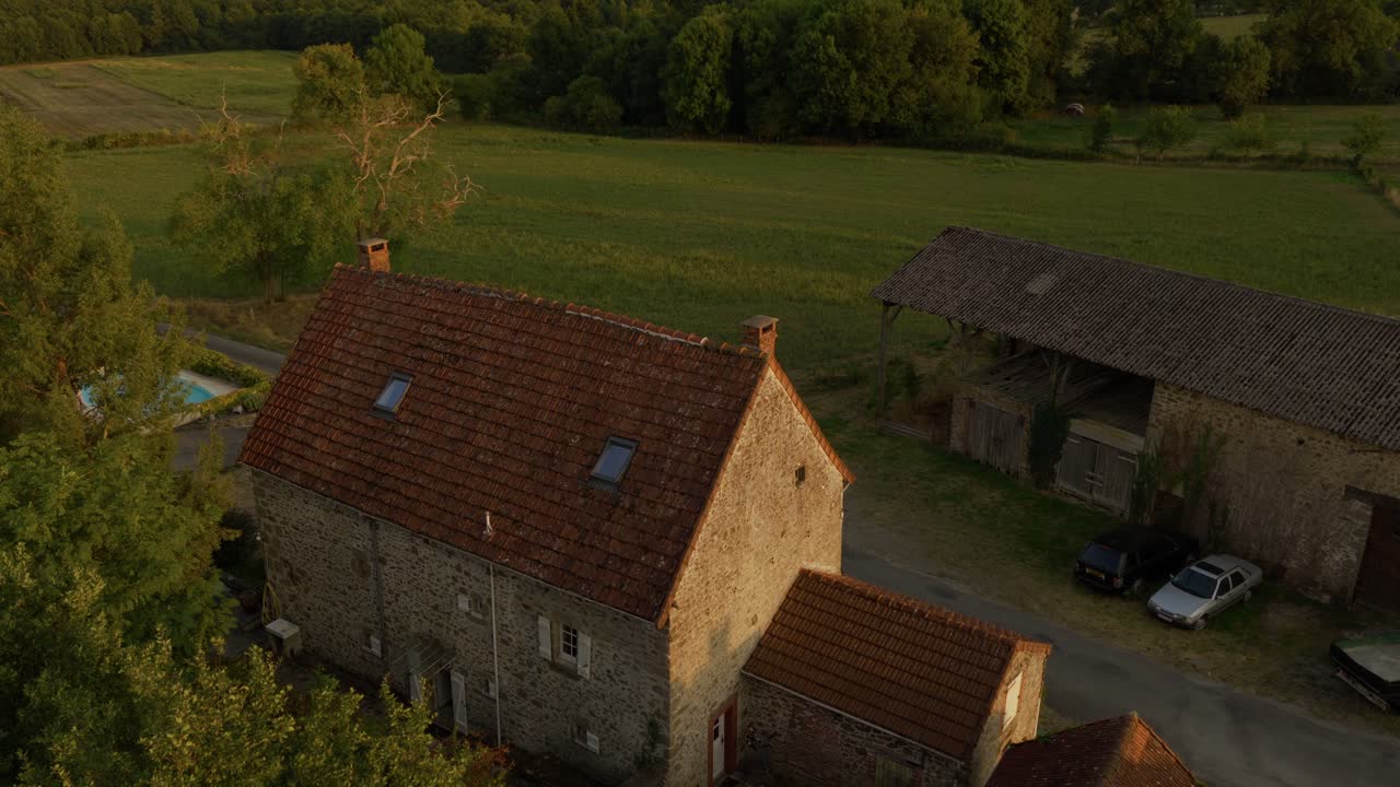 Aerial view of a countryside village with stone houses, barns, and winding roads glowing in warm sunset light