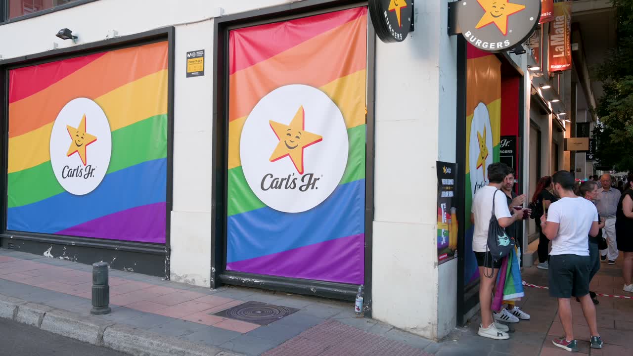 Customers outside the Carl's Jr. fast food restaurant in Madrid, adorned with rainbow flags for LGBTQIA Pride Month.