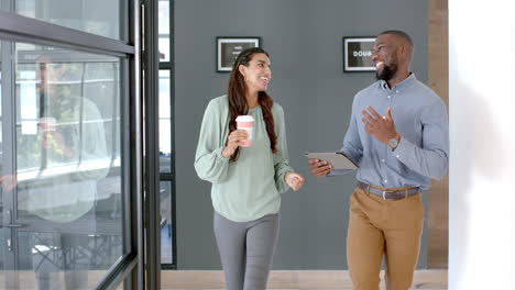 walking in office, colleagues discussing work while holding coffee and tablet