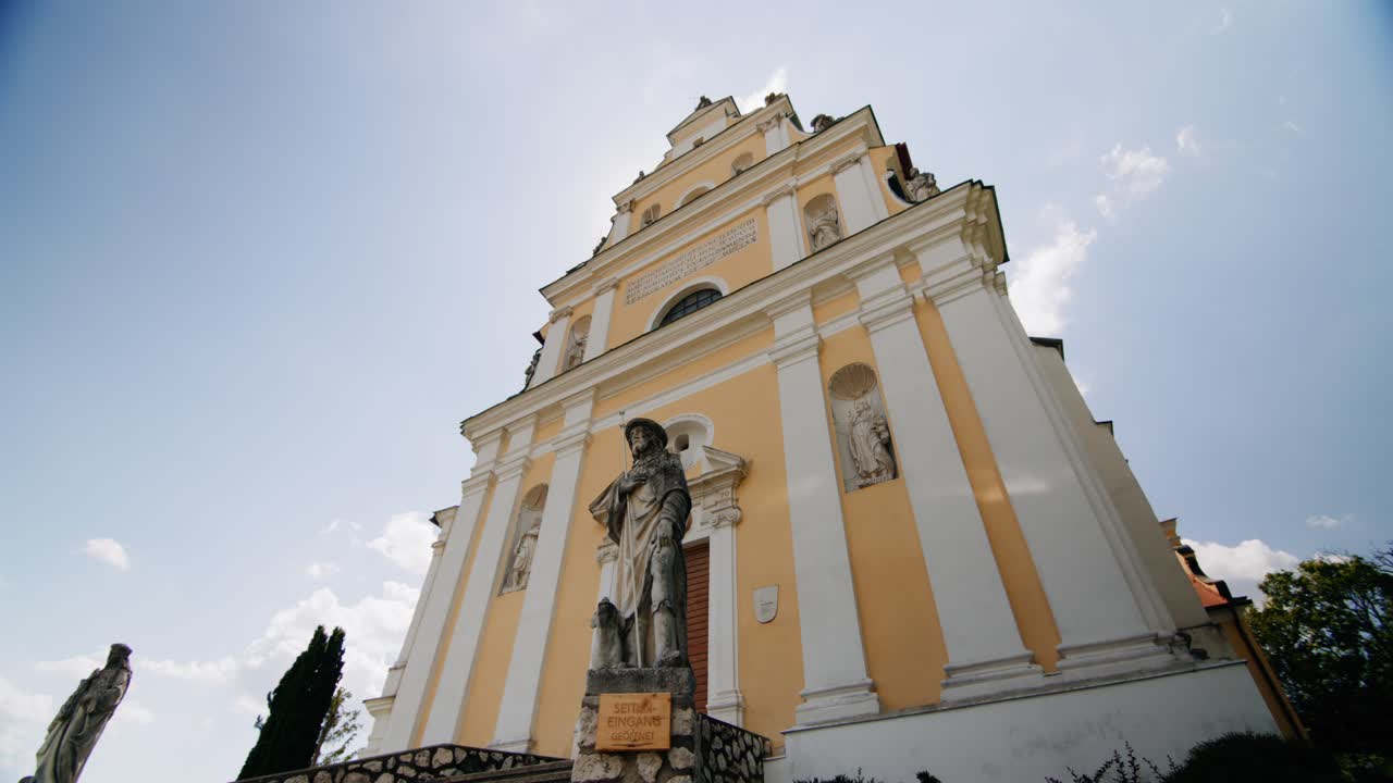 большая старая католическая церковь фалькенштейна с большими каменными статуями спереди панорамирование по фронту здания и показ солнца