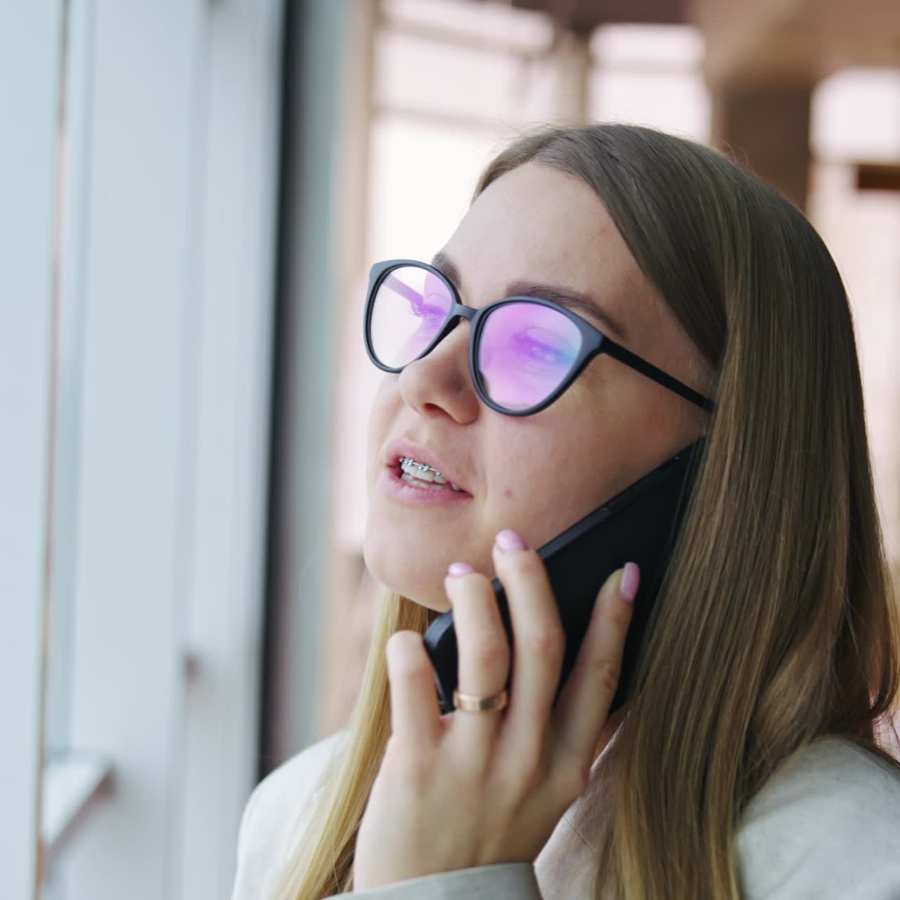 Smiling lady talking on the phone. Close up portrait of a positive young lady standing near big panoramic window