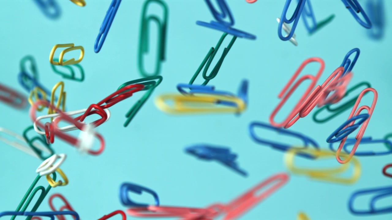 Clips de papel de colores cayendo a cámara lenta sobre un fondo azul.