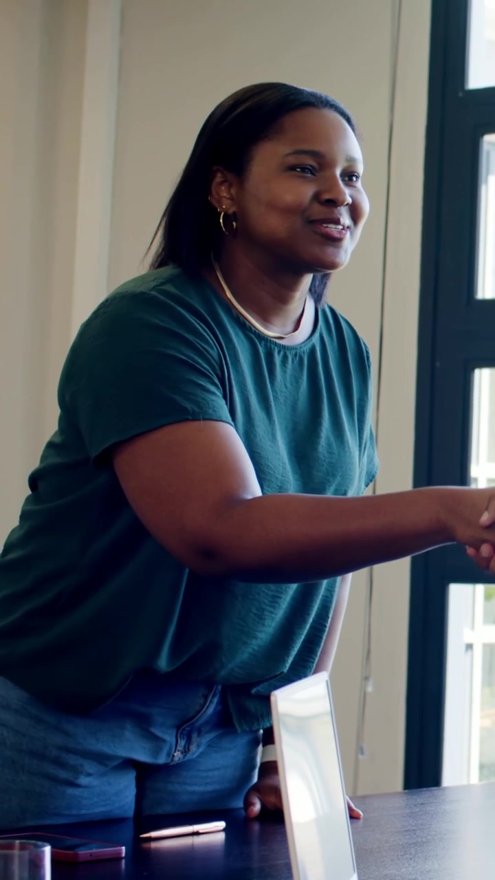 Vertical video: Rising from chair woman in green tee reaching for shake at meeting table, greeting