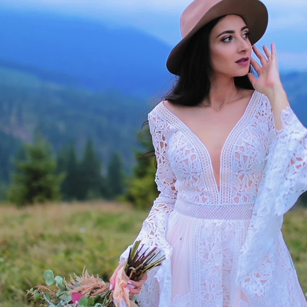 Romantic bride in white dress among nature. Portrait of a beautiful girl in wedding dress and hat on mountain landscape.