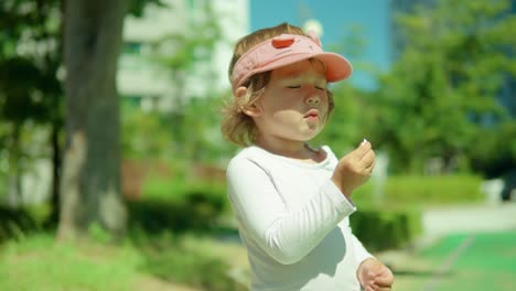 two-year-old girl in trendy outfit eating tasty sweet candy on sunny day outside - middle shot, slow tilt up motion