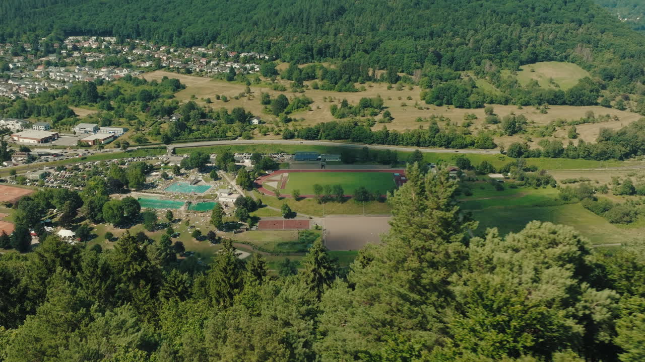 Backward drone fly at green hillside with distant scattered houses and FC Blau Weiss Neckargemünd stadium, Baden-Württemberg, Germany