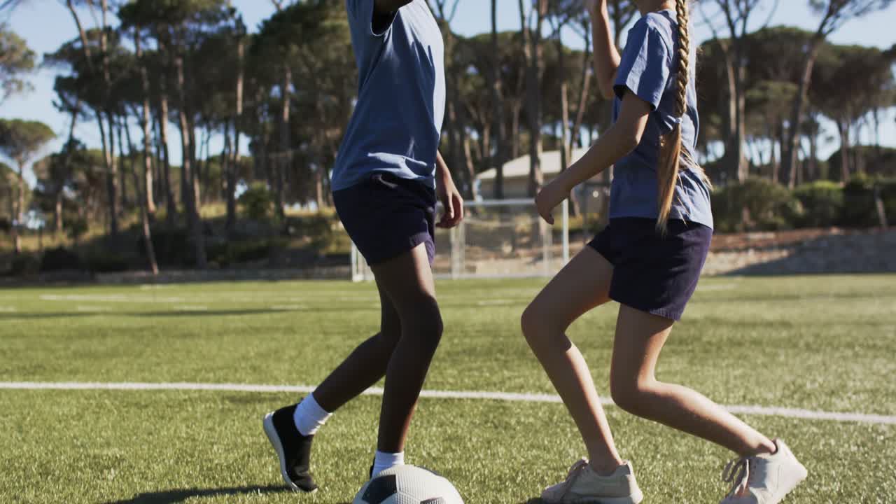 Diversi amici adolescenti che pianificano una partita, si danno il cinque mentre camminano con la palla verso la porta sul campo con kit blu