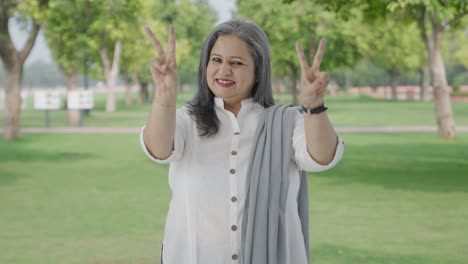 happy indian mother showing victory sign in park