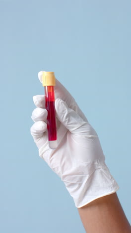 vertical video of hand wearing medical glove holding blood sample on blue background, slow motion