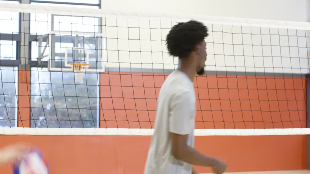 Diverse male team in jerseys planning, stacking hands, starting rally at gym by net with volleyball