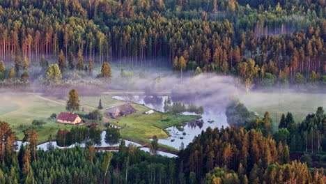 isolated rural house in a wooded valley with fog at dawn. aerial