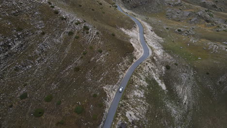 Drone-shot-of-car-driving-through-the-mountains-with-rocks-in-Montenegro