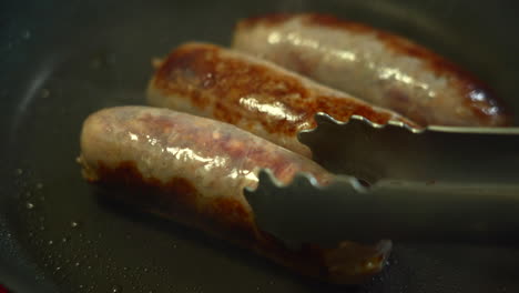 the chef is turning delicious sausages while searing them in a non stick pan