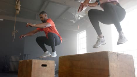 Diverse-group-fitness-class-jumping-onto-boxes,-cross-training-at-gym,-in-slow-motion