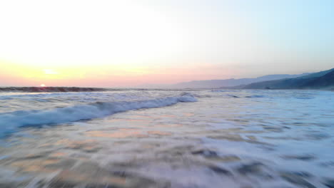 Toma-Aérea-De-Las-Olas-Del-Océano-Rompiendo-En-La-Playa-Bajo-Un-Colorido-Fondo-De-Cielo-De-Puesta-De-Sol-A-Lo-Largo-De-La-Costa-De-Ventura,-Drone-De-California