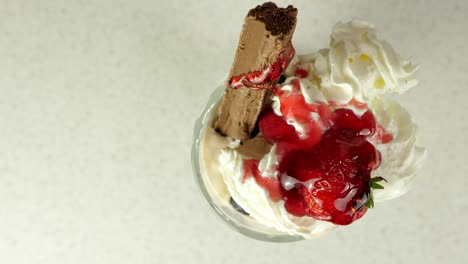 Rociando-De-Arriba-Hacia-Abajo-Jarabe-De-Frutas-Sobre-Un-Helado-Cargado-De-Frutas-Con-Crema-Batida-Y-Una-Barra-De-Chocolate