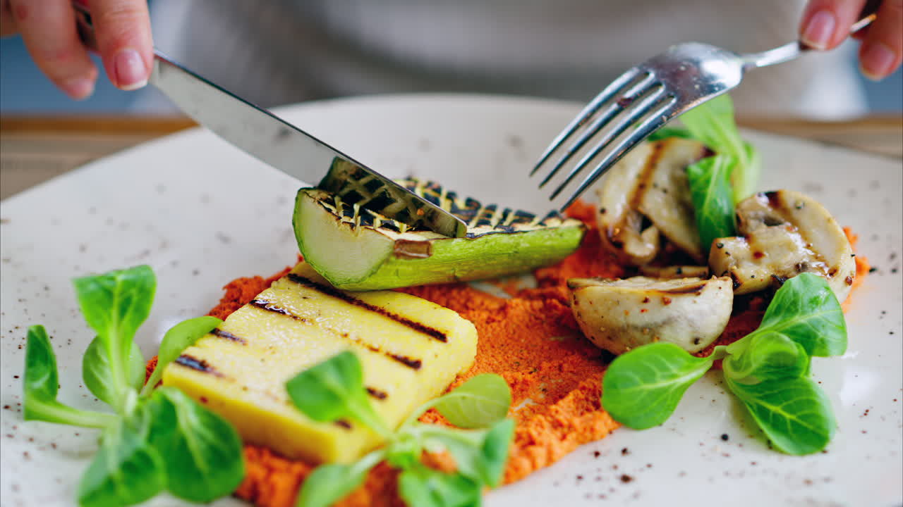 Woman eating grilled zucchini with mushrooms, polenta and hummus