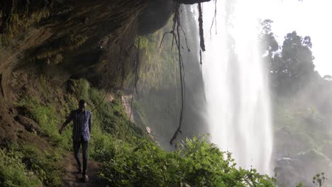 toma en cámara lenta de un hombre africano caminando en una cueva detrás de una cascada tropical