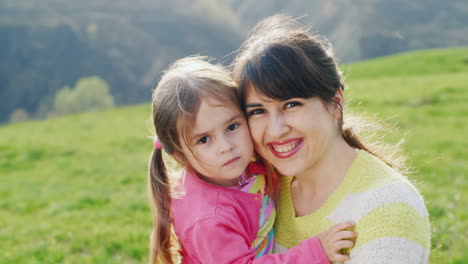 una niña pequeña con dos colas graciosas abraza a su madre y mira a la cámara juntas alegremente