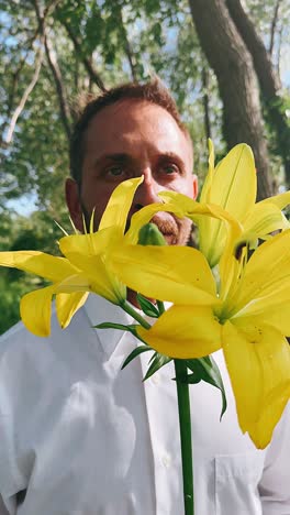 man smelling yellow lilies in a forest