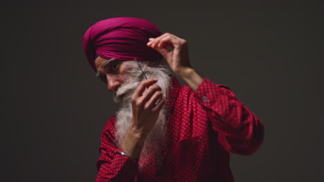 Low-Key-Studio-Lighting-Shot-Of-Senior-Sikh-Man-With-Beard-Tying-Fabric-For-Turban-And-Using-Salai-Needle-Against-Dark-Background-2