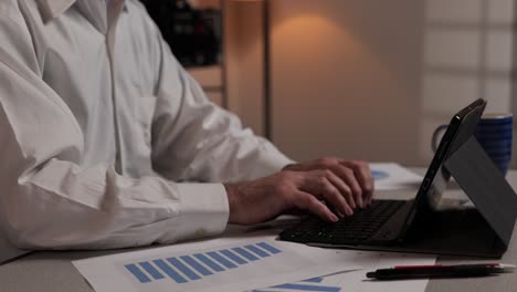 Businessman-types-in-data-on-a-tablet-computer-and-checks-paperwork