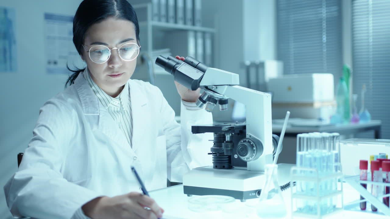 Female Scientist Using Microscope and Taking Notes during Lab Research