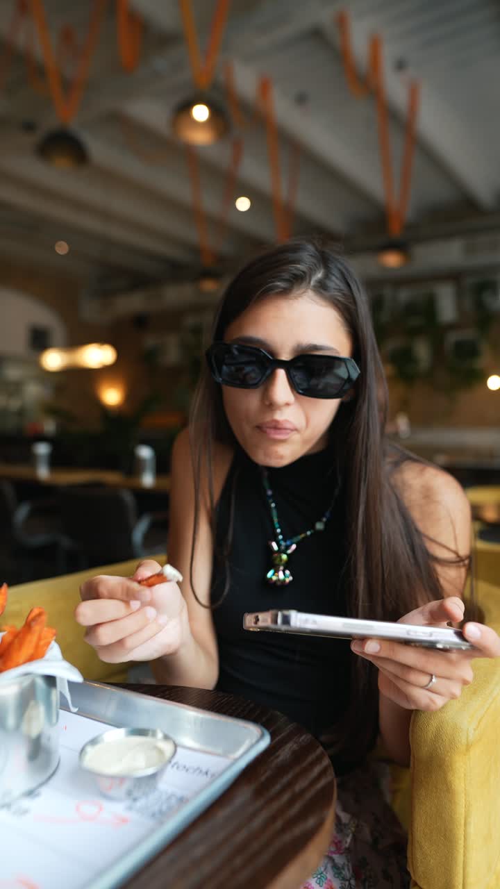 mujer comiendo papas fritas y usando el teléfono en el café