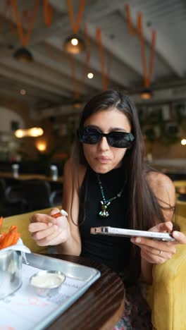 woman eating sweet potato fries and using phone in cafe