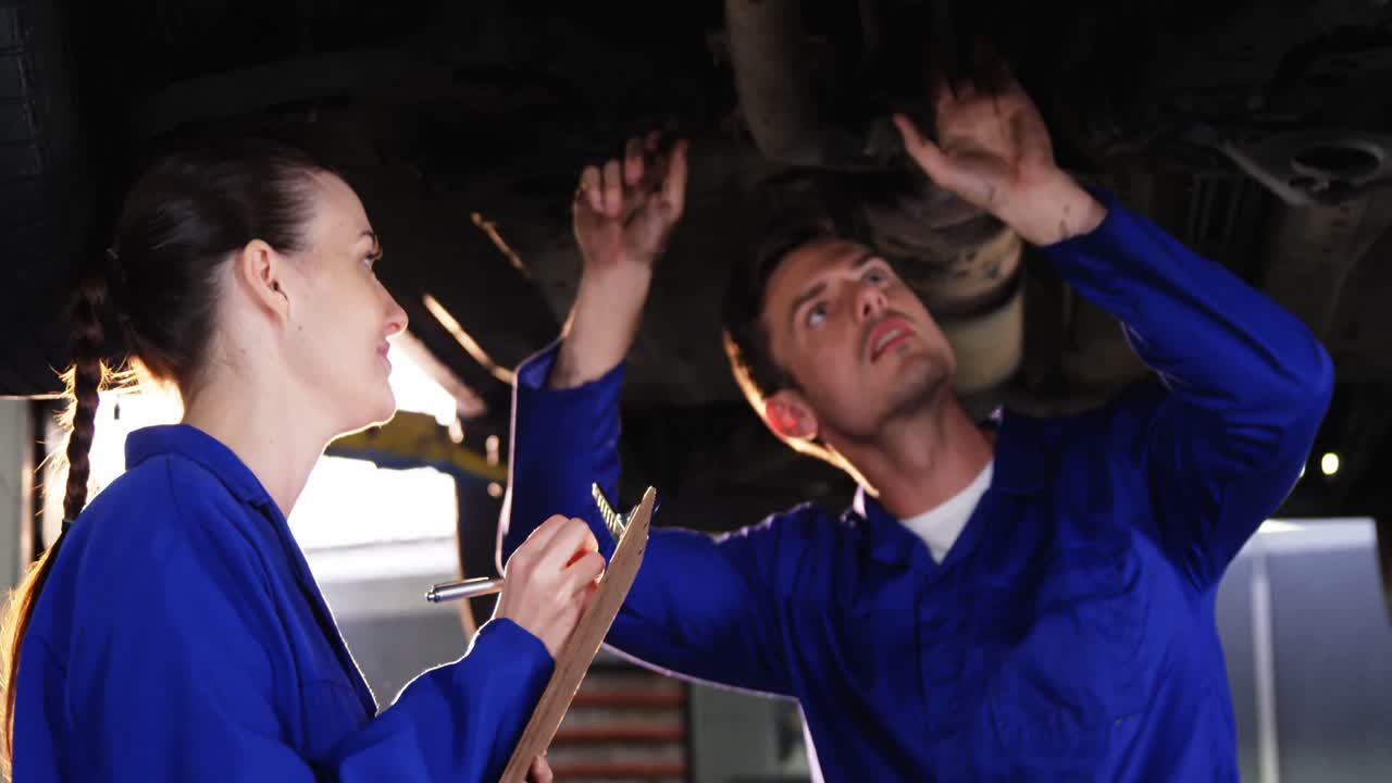 여성 기계공이 클립보드에 글을 쓰고 남성 기계공이 차를 확인하고 있습니다.