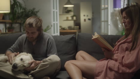 couple resting on sofa with book and dog at home