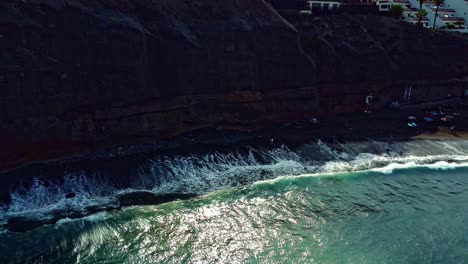 Wellen-Plätschern-Am-Strand-An-Der-Küste-Von-Teneriffa-In-Spanien-Mit-Wohnungen-Auf-Einer-Klippe-Im-Sommer